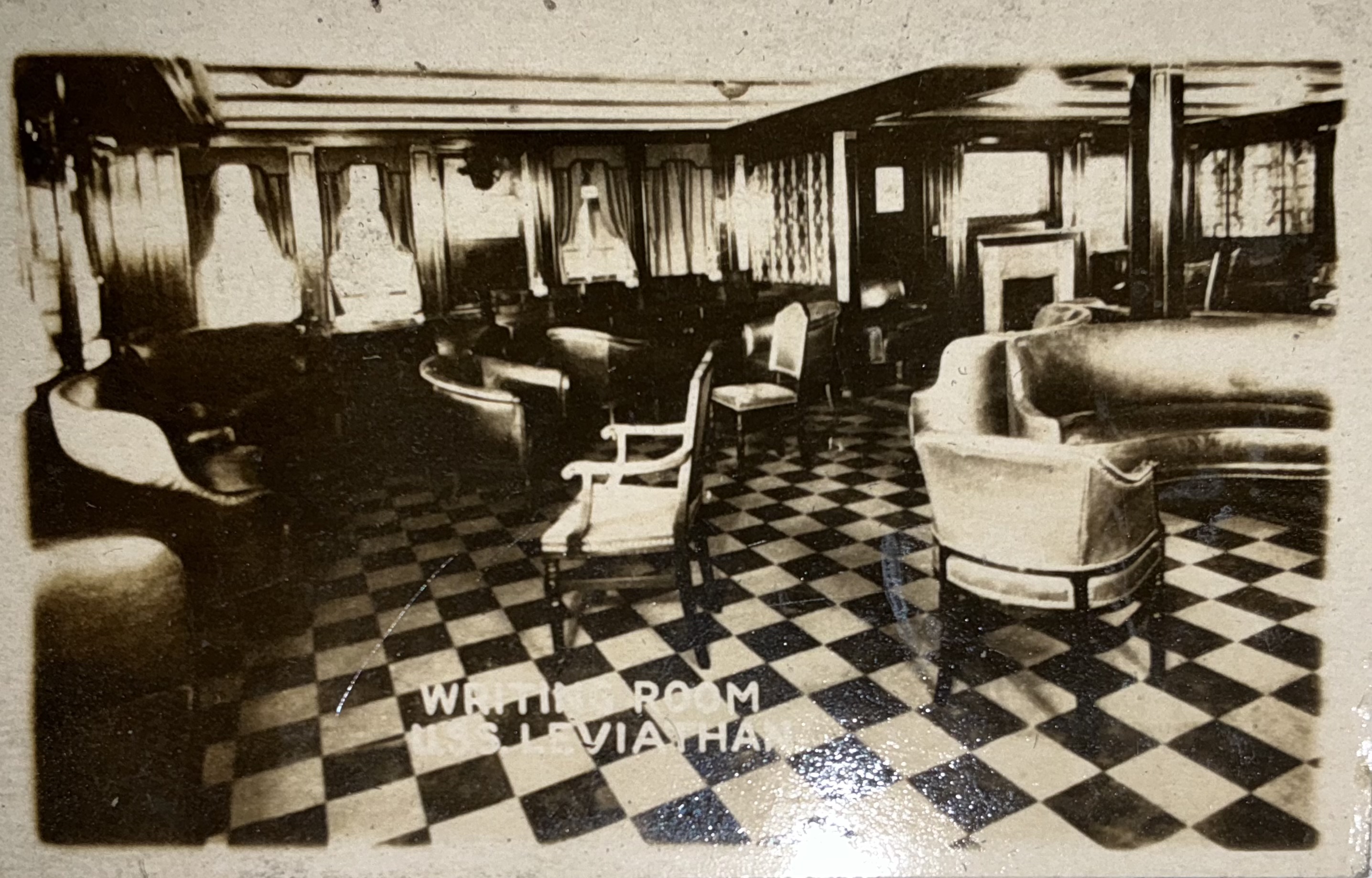 Writing room with upholstered seating, tables and patterned flooring.