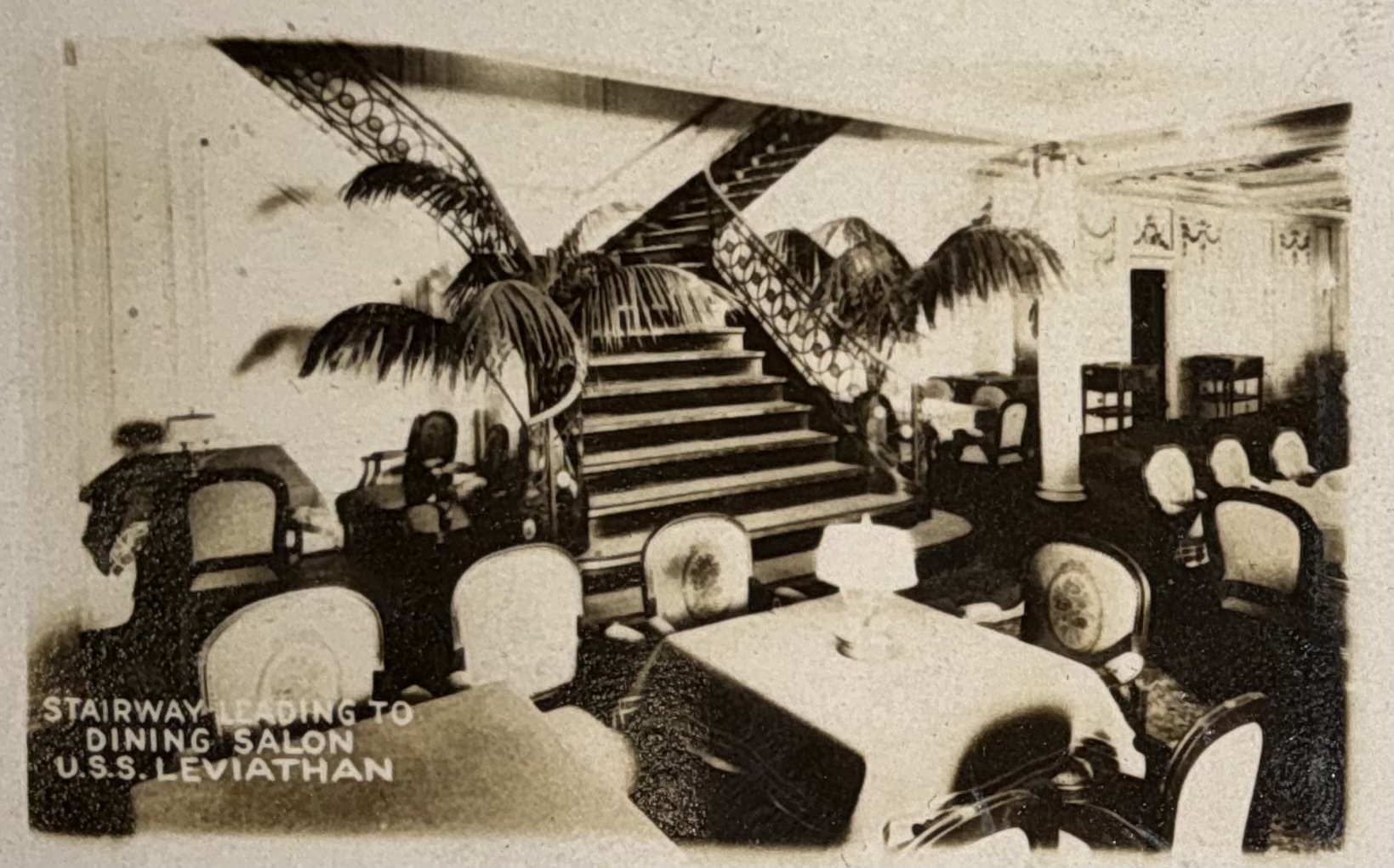 Ornamental stairway and dining furniture framed by palms.