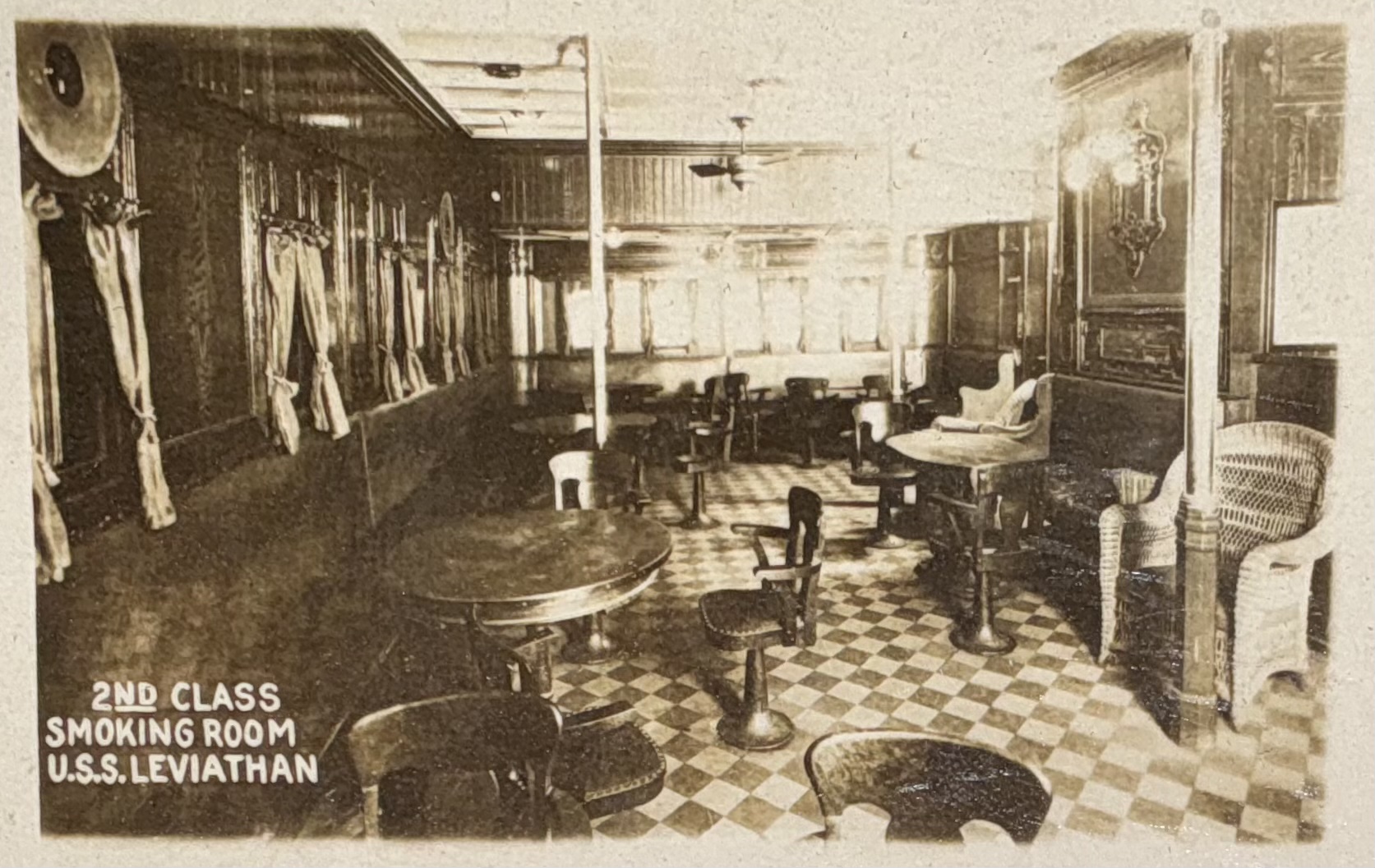 Second-class smoking room with tables and wicker seating.