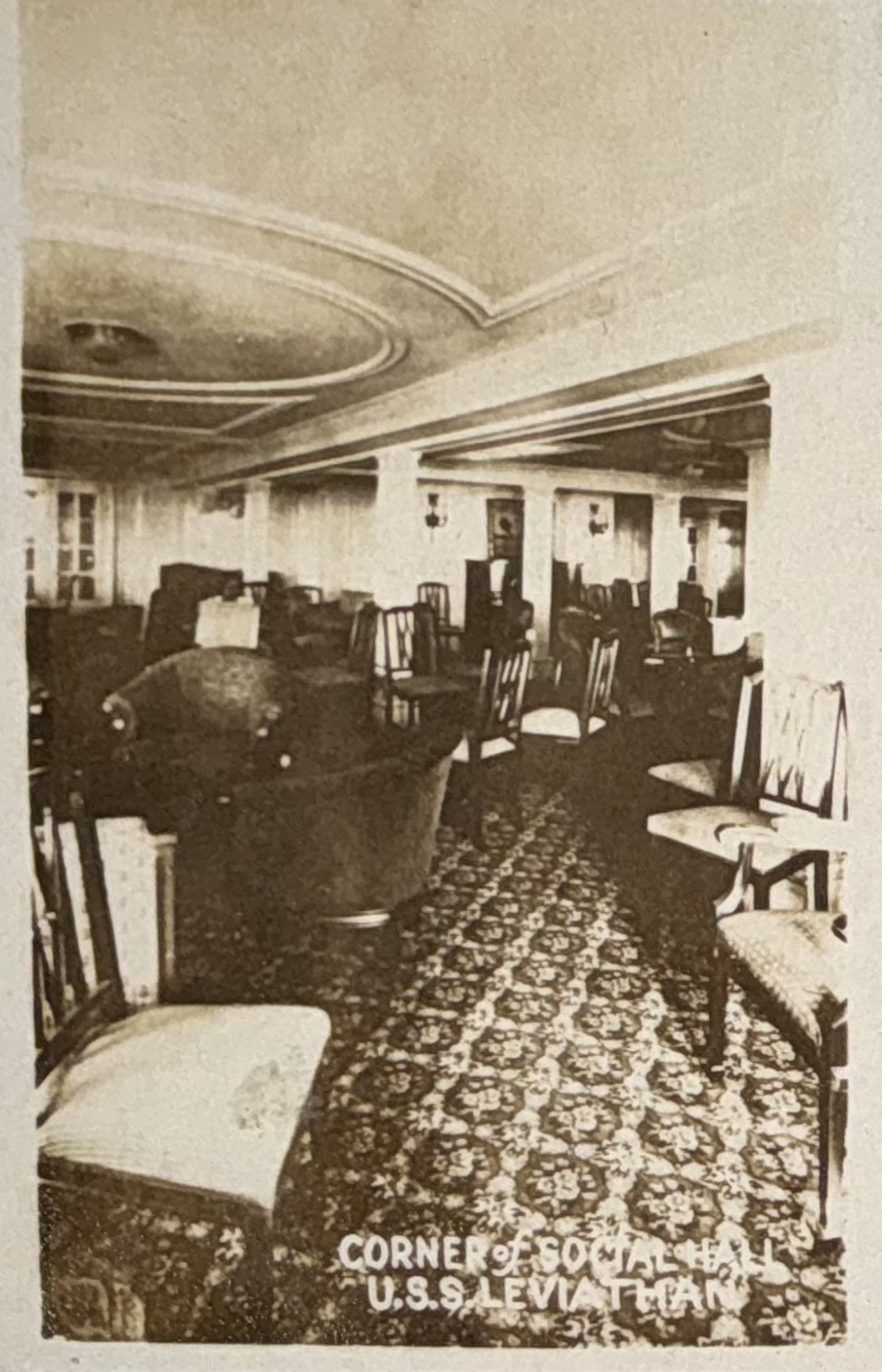 Armchairs and sofas within a carpeted lounge; original caption identifies a corner of the social hall.
